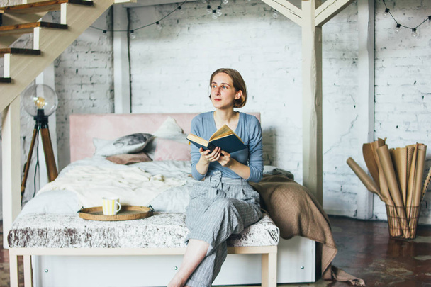 Young woman reading book on bed in loft art work studio room - Foto, imagen