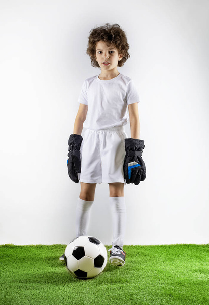 Boy with soccer ball on the green grass. Excited little toddler boy playing football on soccer field against light background. Active childhood and sports passion concept. Save space - Фото, изображение