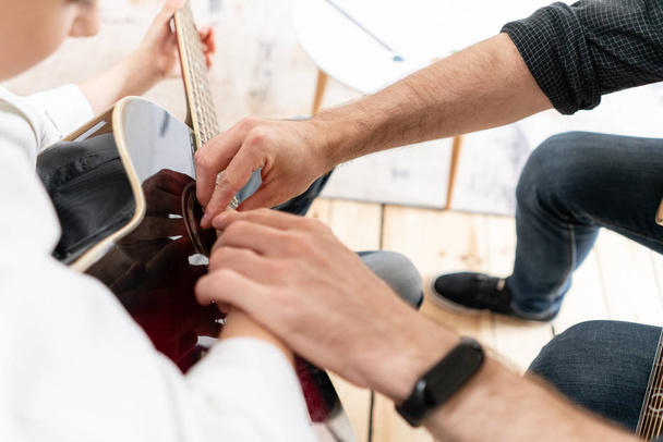 Крупный план руки мальчика в белой рубашке, который учится играть аккорды на гитаре
 - Фото, изображение