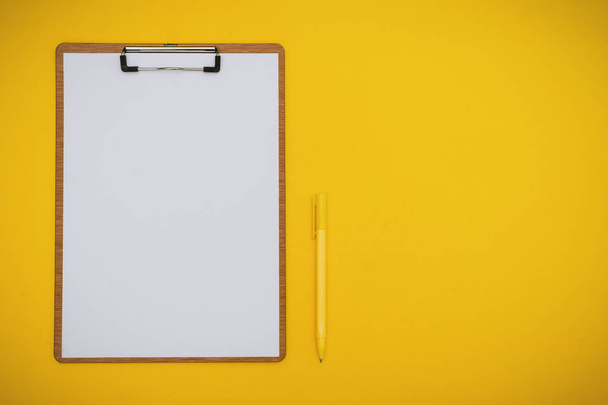 Papel sobre portapapeles y lápiz sobre fondo amarillo
 - Foto, Imagen