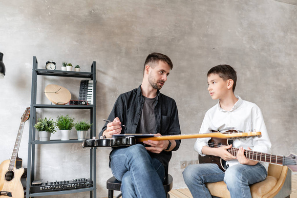 Two brothers of different ages talk to each other after guitar exercise - Foto, afbeelding
