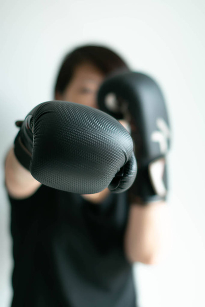 eine Frau in schwarzen Boxhandschuhen, die ihre rechte Faust nach vorne streckt. - Foto, Bild