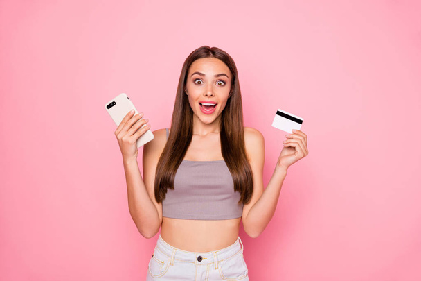 Portrait of impressed lady holding debit card device screaming wow omg wearing stylish trendy tank-top white denim jeans isolated over pink background - Foto, Bild