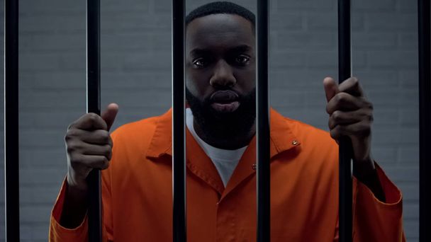 Black prisoner holding bars and looking at camera, drug dealer punishment - Zdjęcie, obraz
