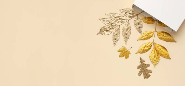 フラットレイクリエイティブな秋の構成。ベージュの背景トップビューコピースペースにホワイトギフトペーパーパッケージとゴールデンリーフ。秋の概念。秋の背景。最小限のコンセプトアイデア、花のデザイン - 写真・画像