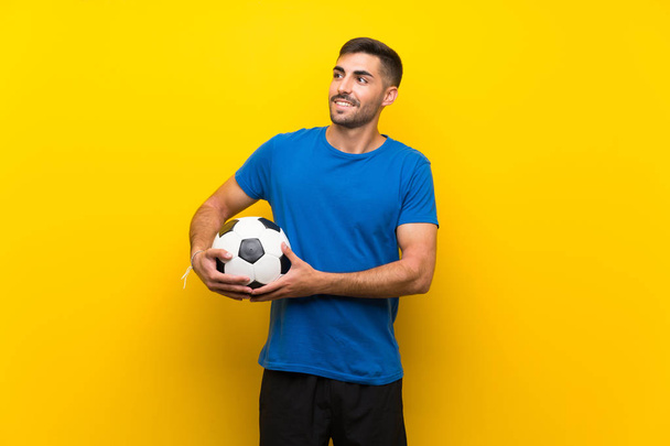 Giovane giocatore di calcio bello uomo oltre isolato muro giallo guardando mentre sorride
 - Foto, immagini