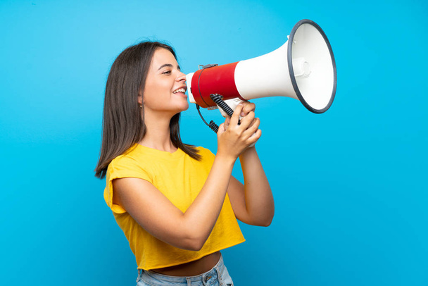 Young girl over isolated blue background shouting through a megaphone - Foto, Imagem