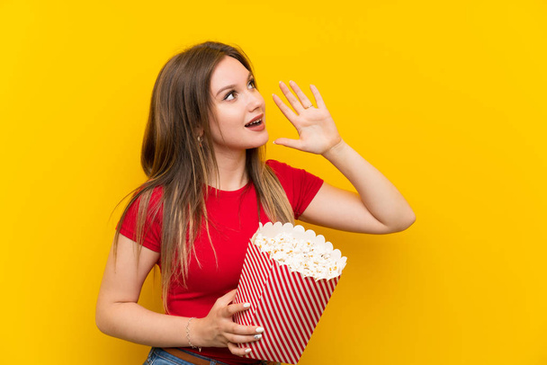 Young woman with popcorns over pink wall shouting with mouth wide open - Foto, Imagem