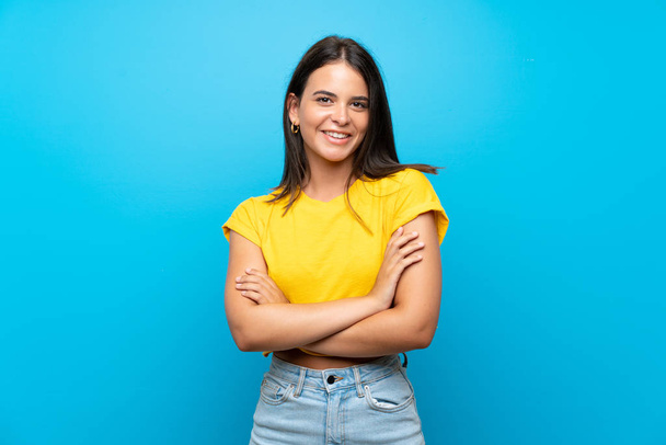 Young girl over isolated blue background keeping the arms crossed in frontal position - Foto, imagen
