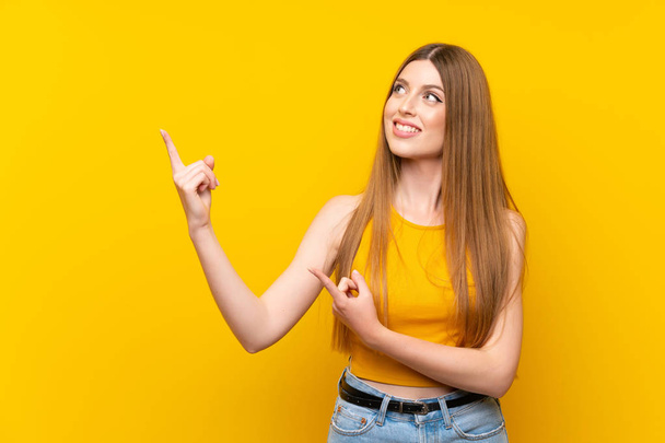 Jonge vrouw over geïsoleerde gele achtergrond wijzend met de wijsvinger een geweldig idee - Foto, afbeelding