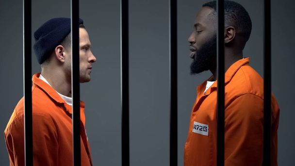 Afro-american and caucasian inmates looking at each other in cell, conflict - Foto, Bild