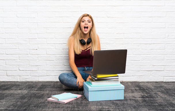 Дівчина-підліток сидить на підлозі зі своїм ноутбуком з несподіваним виразом обличчя
 - Фото, зображення