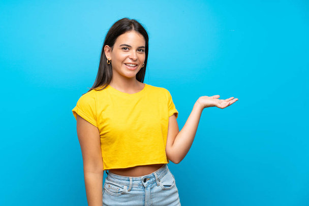 Chica joven sobre fondo azul aislado sosteniendo espacio de copia imaginario en la palma de la mano para insertar un anuncio
 - Foto, imagen