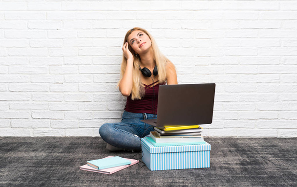Adolescente menina sentada no chão com seu laptop pensando uma ideia
 - Foto, Imagem