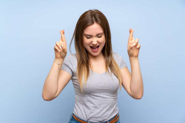 Adolescente sur un mur bleu isolé avec les doigts croisés
 - Photo, image