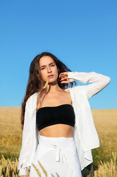 The pretty girl with long hair in stylish white pants and black top and white shirt.Long haired,curly girl.Stylish girl.Girl in rye.Summer photos of a beautiful girl in the field - Foto, Imagem