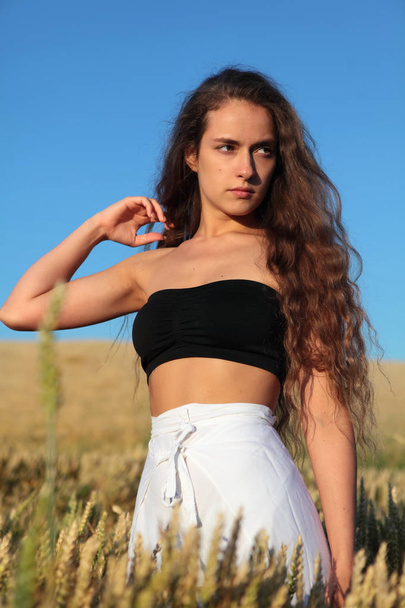 The pretty girl with long hair in stylish white pants and black top .Stylish girl.Girl in rye.Long haired,curly girl.Summer photos of a beautiful girl in the field - Zdjęcie, obraz