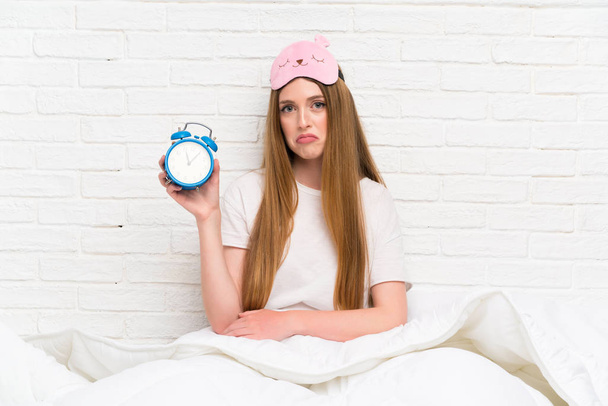 Young woman in dressing gown in bed holding vintage clock - 写真・画像