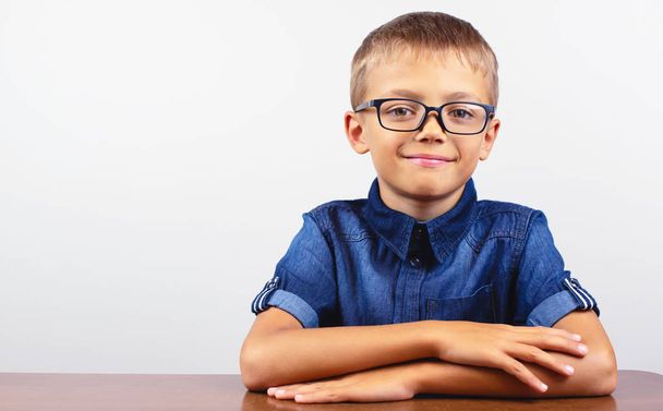 Banner Colegial con una camisa azul sentado a la mesa. Niño con gafas sobre fondo blanco Concepto de vuelta a la escuela
 - Foto, imagen