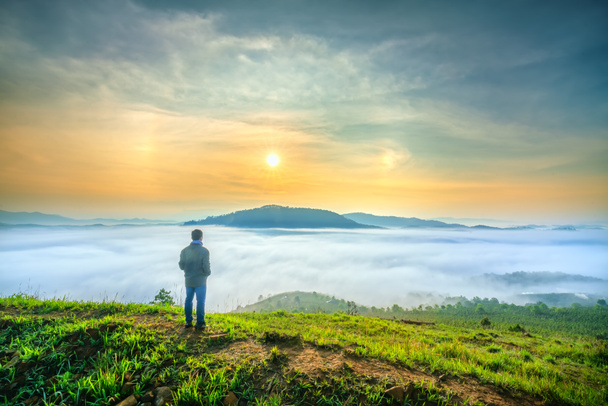 Силуэт человека, стоящего на высоком холме живописного сельского города в утренней долине туман окутанных гор маячит большое волнистое живописное место
 - Фото, изображение