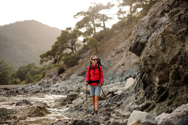 Slim fit woman walk on the rocks on the coastline on the sea with hiking backpack - Foto, afbeelding