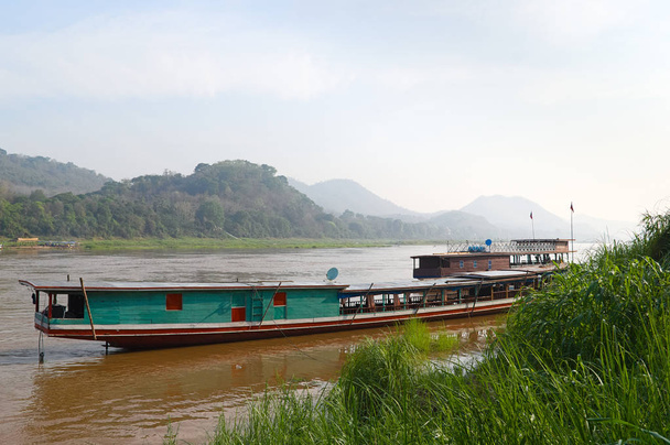 Lunga barca di legno sul fiume Mekong. Caffè galleggiante sulla barca sullo sfondo delle montagne. Luang, Prabang, Laos
. - Foto, immagini