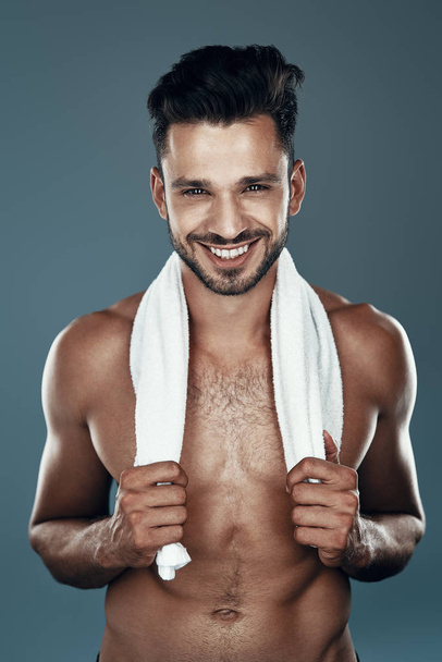 Handsome young shirtless man looking at camera and smiling while standing against grey background - Foto, Imagen