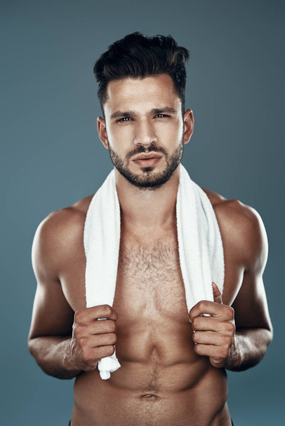 Handsome young shirtless man looking at camera while standing against grey background - Fotó, kép