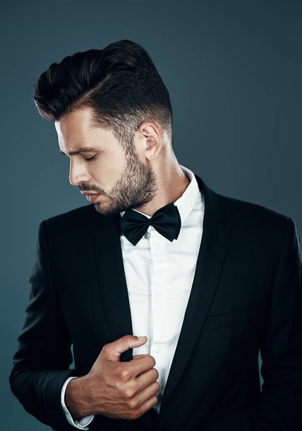 Charming young man in bow tie adjusting jacket while standing against grey background - Photo, Image
