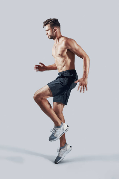 voller Länge von hübschem jungen Mann in Sportkleidung beim Springen vor grauem Hintergrund - Foto, Bild