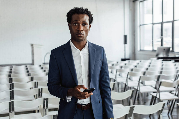 african american businessman in formal wear holding smartphone in conference hall - Fotografie, Obrázek