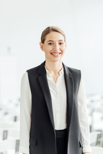 attractive and happy businesswoman in formal wear smiling in conference hall - Foto, Bild
