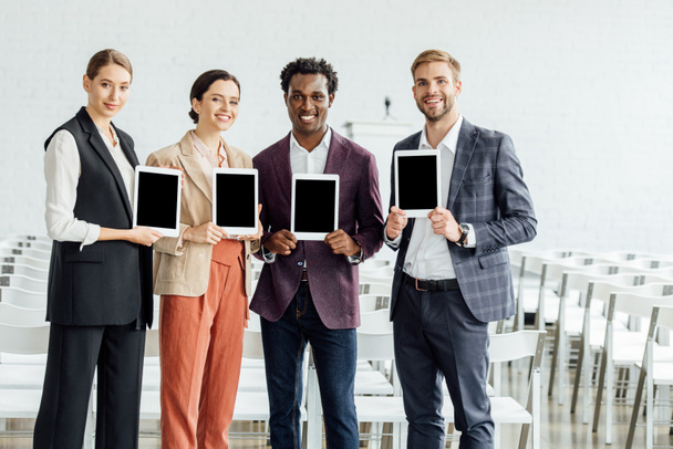 quatro colegas multiétnicos segurando tablets digitais e sorrindo na sala de conferências
 - Foto, Imagem