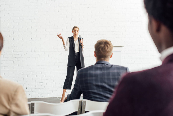 attractive businesswoman holding microphone and talking during conference in conference hall - Photo, Image