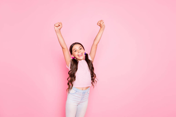 Portrait of cheerful child raising fists screaming yeah dressed white t-shirt pants trousers isolated over pink background - Фото, зображення