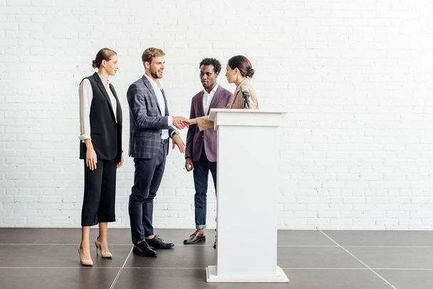 четыре мультиэтнических коллеги в формальной одежде говорить и пожимать руки в конференц-зале
 - Фото, изображение