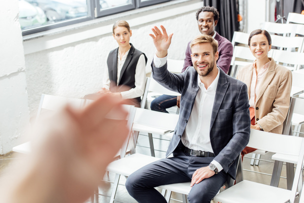 selective focus of businessman raising hand and smiling during conference  - Photo, Image