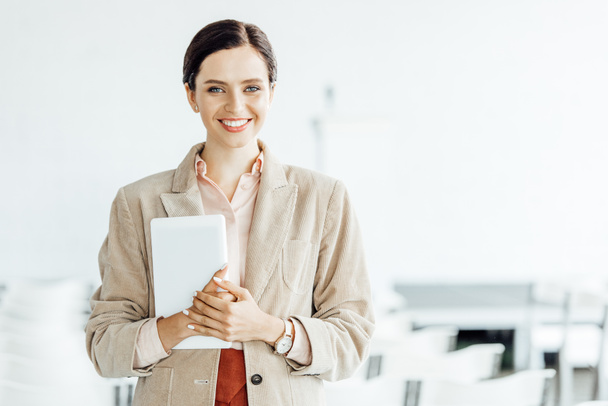 attractive businesswoman in formal wear smiling and holding digital tablet in conference hall - Photo, Image