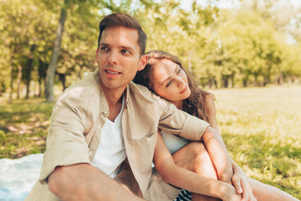 Outdoors image of beautiful couple in love, dating at the park on a sunny day. Happy couple sitting on the blanket at the grass, spending time together, in the nature background. Valentine day.  - Foto, Imagen