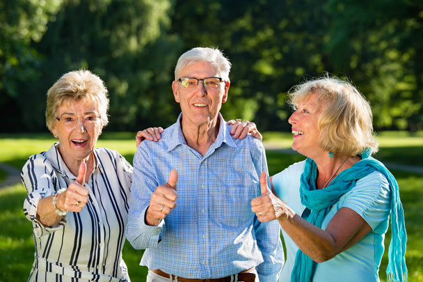 Amici anziani attivi, due donne e un uomo in piedi e mostrando i pollici in su
 - Foto, immagini