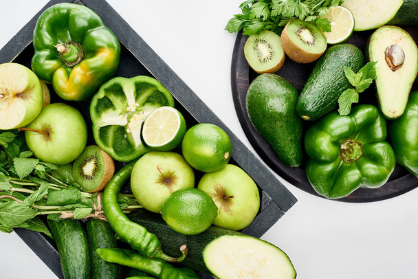top view of avocados, peppers, kiwi, apples, limes, zucchini and greenery on pizza skillet and box  - Foto, imagen