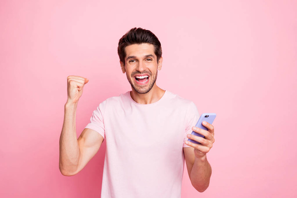 Portrait of his he nice attractive cheerful cheery lucky ecstatic successful confident guy holding in hands device gadget rejoicing having fun isolated over pink pastel background - Zdjęcie, obraz
