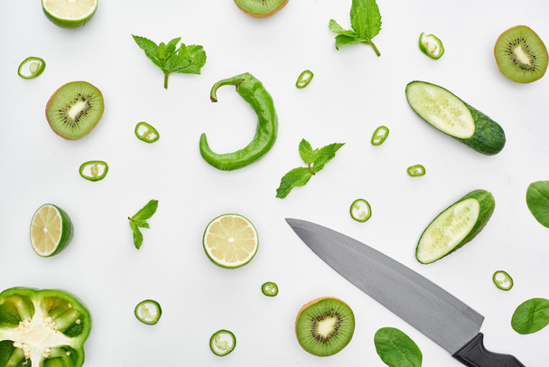  top view of knife, fresh cucumbers, kiwi, limes, peppers and greenery  - Фото, изображение