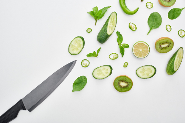  top view of knife, fresh cucumbers, kiwi, lime, peppers and greenery  - 写真・画像