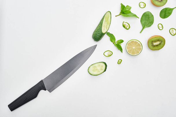  top view of knife, fresh cucumbers, kiwi, lime, peppers and greenery  - Zdjęcie, obraz