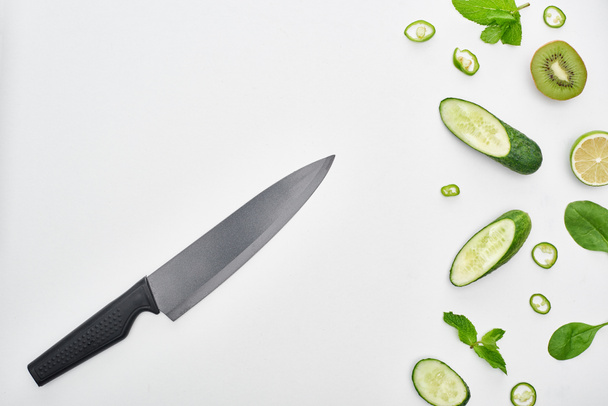  top view of knife, fresh cucumbers, kiwi, lime, peppers and greenery  - Фото, изображение