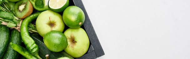 panoramic shot of peppers, kiwi, apples, limes and greenery in wooden box - Photo, Image