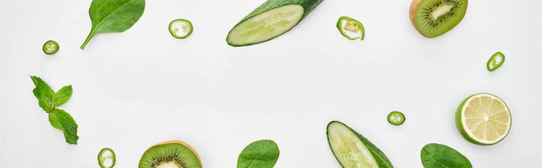 panoramic shot of fresh cucumbers, kiwi, lime, peppers and greenery  - Photo, Image