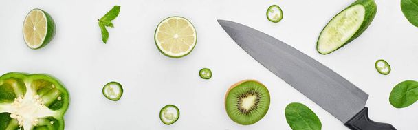  top view of knife, fresh cucumbers, kiwi, limes, peppers and greenery  - Valokuva, kuva