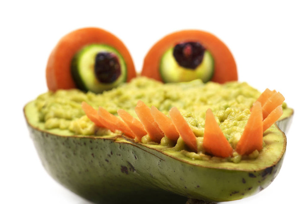 Creative crocodile made of avocado with dip, cucumbers eyes and teeth made of carrots isolated on white background - 写真・画像